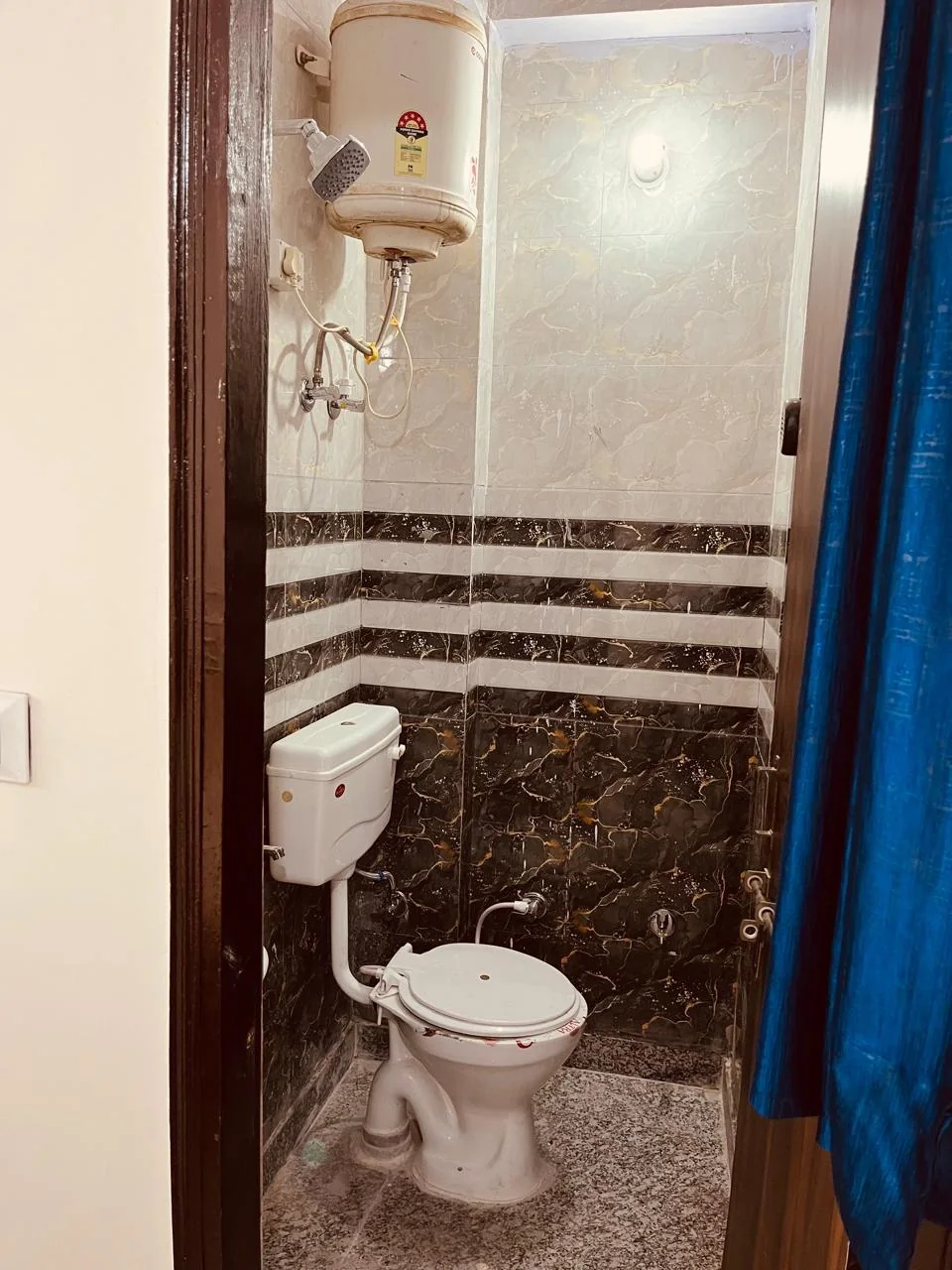 A tiled bathroom with a shower, toilet and blue curtain.