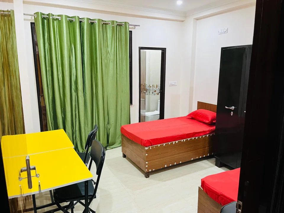 Two beds and yellow study tables in a room with green curtains.